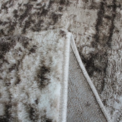Tapete cinza e branco com padrão abstrato e textura felpuda dobrado mostrando o verso.