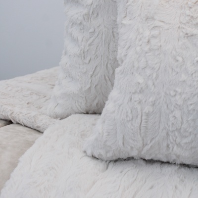 Almofadas e manta peludas brancas sobre superfície bege