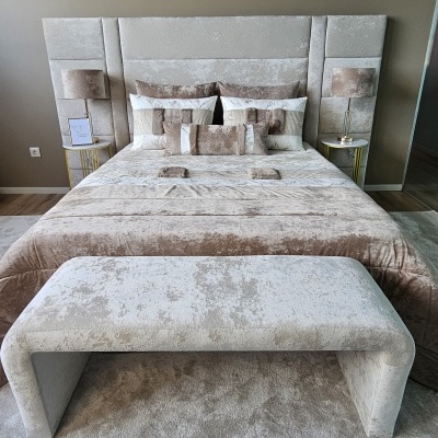Quarto com cama estofada bege claro e mesa de cabeceira com candeeiro