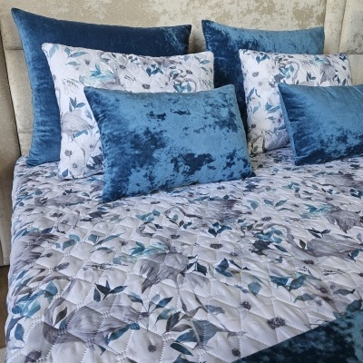 Almofadas azul veludo e branco floral com edredão combinado numa cama