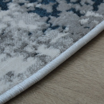 Tapete cinzento e branco com padrão abstrato e borda azul clara no chão de madeira