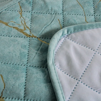 Colcha azul clara acolchoada com detalhes dourados e remate bordado