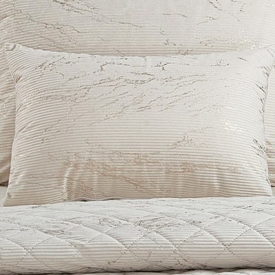 Conjunto de almofadas e colcha creme com padrão texturizado em cama