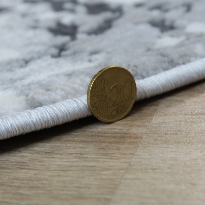 Moeda de 20 cêntimos ao lado da borda de tapete cinzento e chão de madeira.