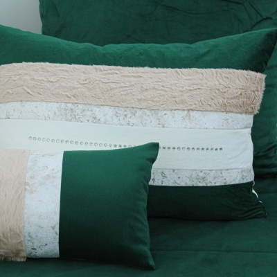 Duas almofadas decorativas com faixas de várias texturas e cores sobre sofá verde escuro