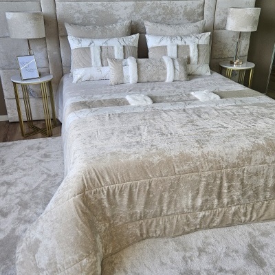 Cama de casal estofada com roupa de cama bege e branca e mesas de cabeceira com candeeiros em quarto