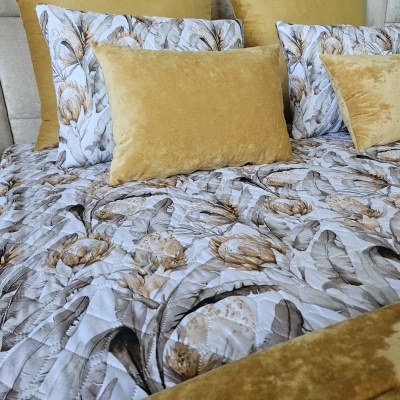 Conjunto de almofadas e colcha floral com almofadas mostarda em veludo numa cama.