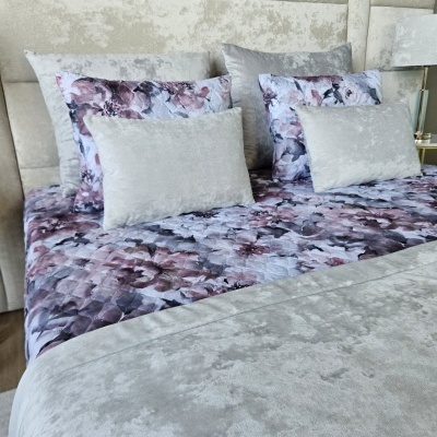 Conjunto cama com edredão floral roxo, almofadas cinzentas e cabeceira aveludada cinzenta