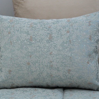 Almofada decorativa retangular azul claro com padrão bege sobre sofá azul com almofada bege.