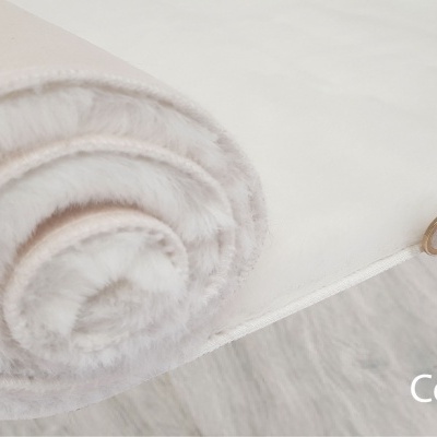 Rolo de tecido branco macio parcialmente desenrolado no chão cinza claro com moeda para escala.