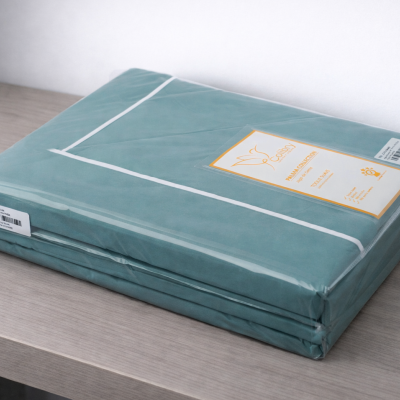 Pack de três lençóis de cama verdes embalados em plástico transparente com etiqueta branca e laranja