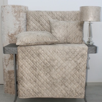 Conjunto têxtil bege de veludo com padrão de losangos numa mesa metálica com candeeiro