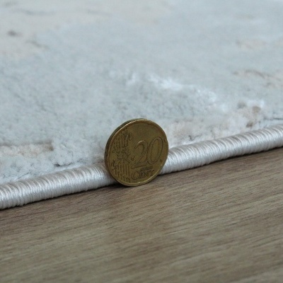 Moeda de 20 cêntimos encostada na borda de tapete branco sobre chão madeira