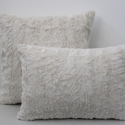 Duas almofadas peludas brancas, uma retangular e outra quadrada, texturizadas, sobre superfície cinza