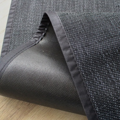 Tapete preto com bordas costuradas sobre chão de madeira clara