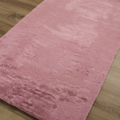 Tapete retangular cor-de-rosa com textura macia sobre chão de madeira claro