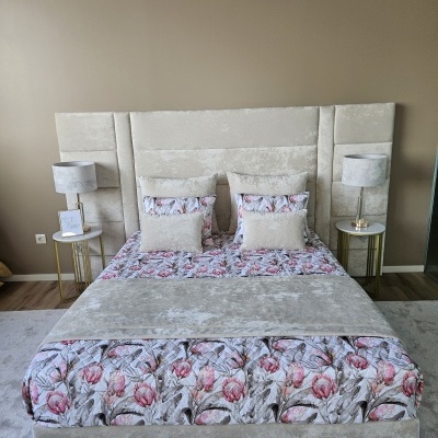 Cama estofada bege com edredão floral, mesas de cabeceira com candeeiros e placa Colibry