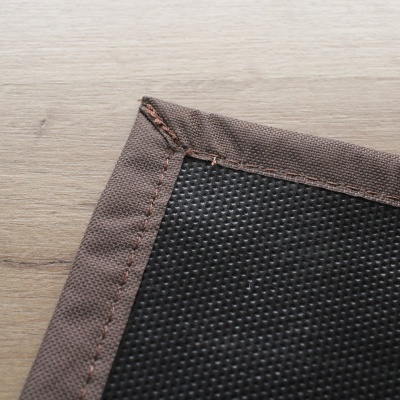 Detalhe de tecido preto texturizado com borda castanha costurada