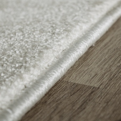 Detalhe de tapete branco felpudo com borda rebordada em chão de madeira clara