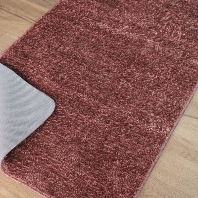 Tapete vinho retangular com pelo curto e base antiderrapante cinza sobre chão de madeira.