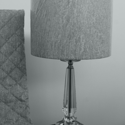 Candeeiro de mesa com base de vidro e abajur cinzento junto a tecido cinzento com padrão