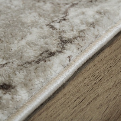 Borda de tapete cinza claro com padrão mesclado sobre chão de madeira clara.