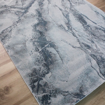 Tapete cinza e azul com padrão abstrato sobre chão de madeira clara