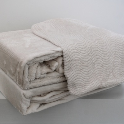 Edredão ou manta bege claro dobrada com padrão ondulado sobre fundo branco.