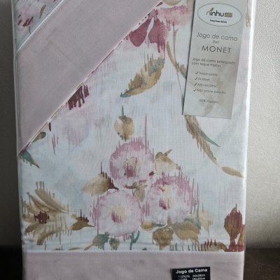 Embalagem de jogo de cama estampado com flores em tons rosa, bege e verde e etiqueta com informações.