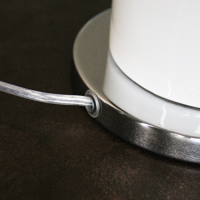 Base de aparelho branco com acabamento inox e cabo transparente sobre superfície escura