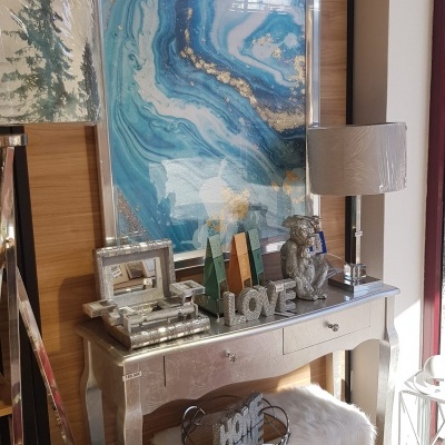 Consola prateada com enfeites LOVE e HOME, duas lâmpadas, cadeira felpuda branca e dois pufes azuis em sala iluminada.