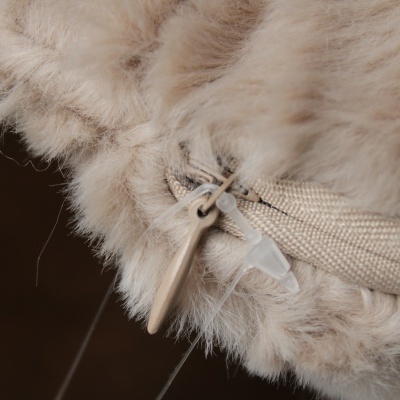 Detalhe de posição de fecho zip em tecido peludo bege com puxador de madeira