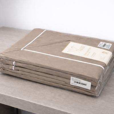 Conjunto de roupa de cama bege embalado em plástico sobre mesa cinzenta