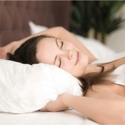 Mulher a dormir numa cama com almofadas e roupa de cama brancas