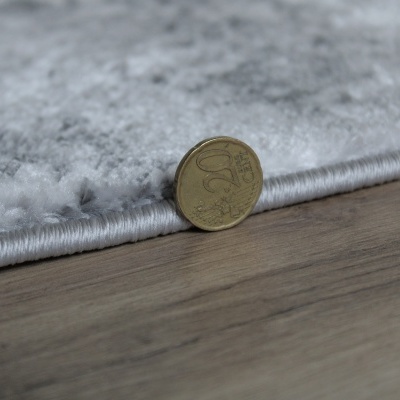 Tapete cinzento com padrão abstracto ao lado de moeda de 20 cêntimos sobre chão de madeira