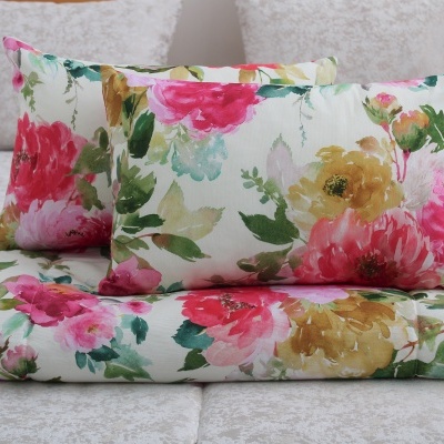 Almofadas e manta com padrão floral colorido sobre cama cinza claro.