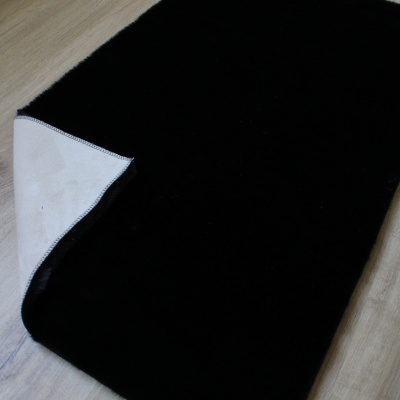 Tapete preto retangular com verso branco em piso de madeira clara