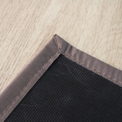 Canto de tapete com base preta e borda castanha sobre chão de madeira clara.