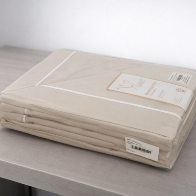 Lençol bege embalado em plástico com etiqueta, sobre superfície cinza clara