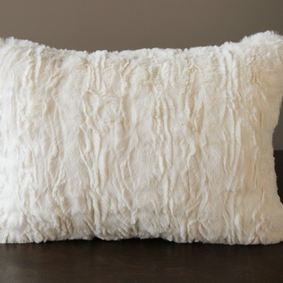 Almofada rectangular creme felpuda sobre superfície escura com fundo cinza