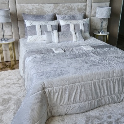 Cama estofada cinzenta com roupa de cama cinza e branco, duas mesas de cabeceira com candeeiros cinza.