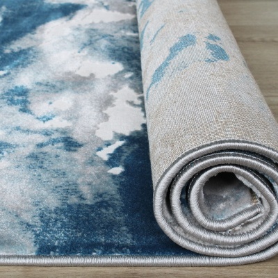 Tapete azul e branco com padrão abstrato parcialmente desenrolado sobre chão de madeira