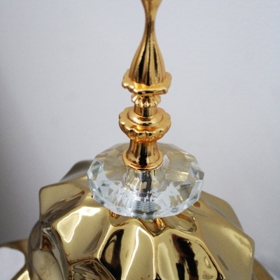 Tampa dourada facetada com puxador decorativo dourado e base de cristal.