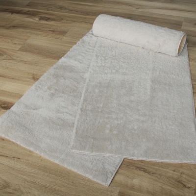 Tapete felpudo branco parcialmente enrolado em chão de madeira clara