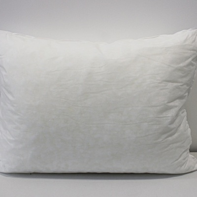 Almofada branca retangular sobre superfície branca e parede cinzenta.