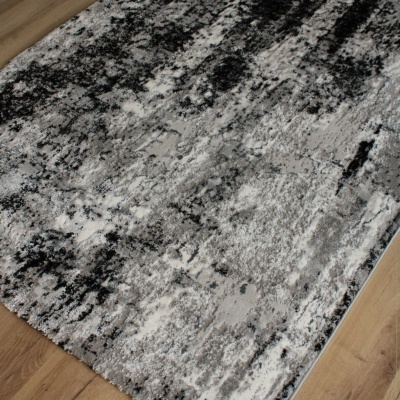 Tapete com padrão abstrato cinza, branco e preto sobre chão de madeira clara