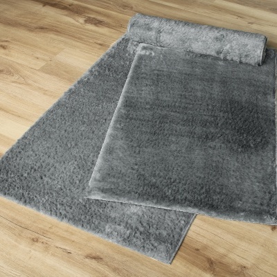 Tapete cinza felpudo parcialmente enrolado em chão de madeira clara