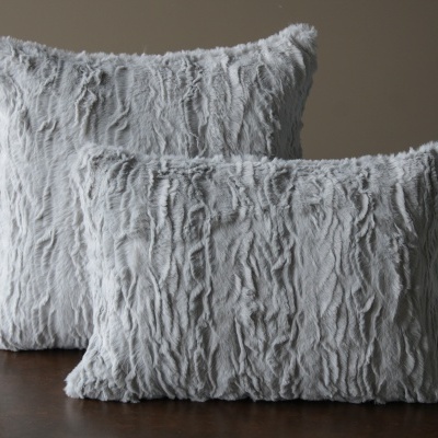 Duas almofadas cinza claras felpudas com textura ondulada sobre mesa de madeira.