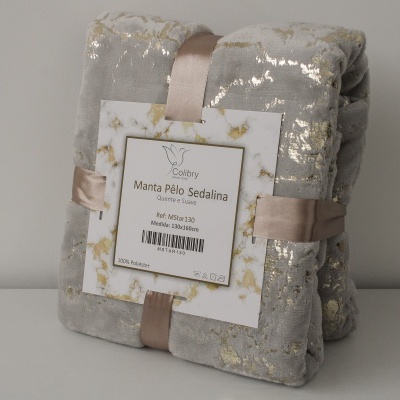 Manta cinzenta com padrão dourado, embalada com fita e etiqueta branca