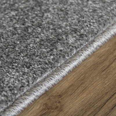 Tapete cinzento felpudo com borda enrolada sobre chão de madeira